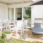 Terrasse mit Esstisch, Stühlen und Liegestuhl unter Sonnenschirm.