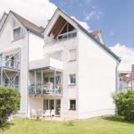 Wohnhaus mit Balkonen und Garten. Weiße Fassade, blauer Himmel.