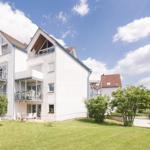 Weiße Mehrfamilienhaus mit Balkonen und grünem Rasen unter blauem Himmel.