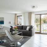 Wohnzimmer mit grauem Sofa, zwei Stühlen und Blick auf Terrasse.