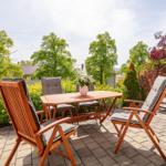 Terrasse mit Holztisch, Stühlen und Liegen. Umgeben von grünen Bäumen und Sträuchern.
