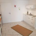 Küche mit weißen Schränken, Arbeitsplatte und Spüle. Holztisch und Teppichboden.