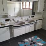 Badezimmer mit zwei Waschbecken, Spiegelschrank und buntem Teppich auf dunklem Boden.