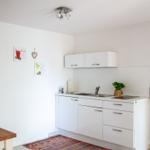 Küche mit weißen Schränken, Spüle und Kochfeld. Wandbild und Teppich sind sichtbar.