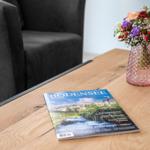 Auf dem Tisch liegt eine Zeitschrift und ein Blumenstrauß in einem Vasen.