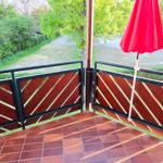 Terrasse mit rotem Sonnenschirm und Holzgeländer. Blick auf grüne Wiesen und Bäume.