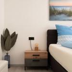 Schlafzimmer mit Bett, Nachttisch und Wandbild. Dekorative Pflanze und Lampen.