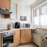 Küche mit Holzschränken, Herd, Kaffeemaschine und Fenster mit Vorhängen.