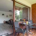Terrasse mit Tisch und Stühlen, Blick in Wohnzimmer mit Sofa und Wanduhr.