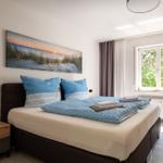 Schlafzimmer mit Bett, Wandbild und Fenster mit Blick auf Grün.