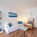 Wohnzimmer mit Sofa, Sessel und Holzboden. Wandbild und Regal mit Dekoration.