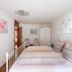 Schlafzimmer mit weißem Metallbett, Wandbild mit Blumen und Schmetterlingsaufklebern an der Wand.