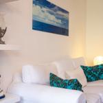 Weißes Sofa mit zwei türkisfarbenen Kissen. Wandbild zeigt Meer und Himmel. Neben dem Sofa steht eine Lampe.