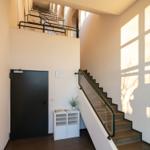 Treppe mit Glasgeländer führt zur oberen Etage. Schwarze Tür und weißer Schrank stehen im Flur.
