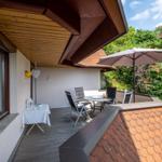 Terrasse mit Tisch, Stühlen und Sonnenschirm. Holzdecke und umliegende Grünflächen.