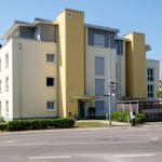 Moderne Wohnhausfassade mit gelben und grauen Akzenten, Eingangsbereich und Fahrrad.