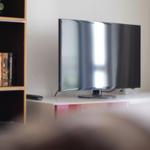 Flachbildfernseher auf weißem Möbelstück neben Bücherregal mit DVDs.