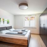Schlafzimmer mit Doppelbett, Kleiderschrank und Fenster mit Blick auf Wohnhaus.