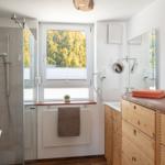 Badezimmer mit Dusche, Waschbecken und Fenster mit Blick auf Bäume.