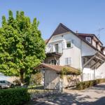 Ein zweistöckiges Haus mit Balkon, umgeben von Bäumen und einem Zaun.