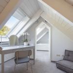 Schlafzimmer mit Dachbodenfenster, Schreibtisch und Sofa. Blick in Schlafbereich.