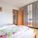 Schlafzimmer mit Bett, Spiegelschrank und Holzboden. Tür führt in angrenzenden Raum.