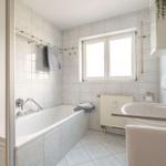 Bad mit Badewanne, Waschbecken und Fenster. Fliesenwand und -boden.
