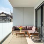 Terrasse mit Sitzgruppe, Tisch und Stuhl. Glasgeländer und Blick auf Nachbarhaus.