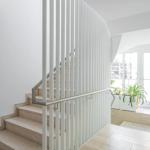 Treppenhaus mit Holztreppe, weißem Geländer und Pflanzen an Fenster