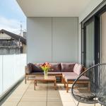Terrasse mit Sitzgruppe, Tisch und Stuhl. Glasgeländer und Blick auf Nachbarhaus.