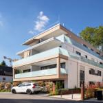 Moderne Mehrfamilienhaus mit Balkonen und Terrasse. Ein weißer Wagen parkt vor dem Gebäude.