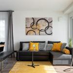 Wohnzimmer mit schwarzer Couch, gelbem Teppich und Wandbild.