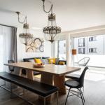 Essbereich mit Holztisch, schwarzen Bänken und zwei Kronleuchtern. Wohnbereich mit Sofa und Balkon.