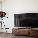 TV auf Holzregal, daneben Stehlampe mit kupferfarbenem Schirm.