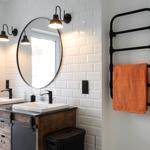 Badezimmer mit zwei Waschbecken, runden Spiegel und Handtuchwärmer mit orangefarbenem Handtuch.