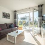 Wohnzimmer mit Sofa, Couchtisch und TV. Durchgang zur Terrasse mit Gartenmöbeln.