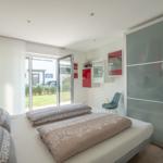 Schlafzimmer mit Bett, Schrank und Glasfront. Durchgang zur Terrasse mit Blick auf Garten.