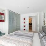 Schlafzimmer mit Doppelbett, Glaswand-Schrank und rotem Kunstwerk an der Wand.