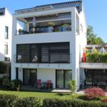 Modernes Haus mit Balkon, Terrasse und Garten. Schwarze Fensterläden und weiße Fassade.