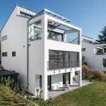 Moderne weiße Villa mit Balkon und Garten. Poolbereich und Terrasse sichtbar.