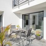 Terrasse mit Tisch, Stühlen und Palme. Glasfront öffnet zum Innenraum.