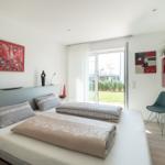 Schlafzimmer mit Bett, Kunst an den Wänden und Blick auf einen Garten.