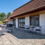 Terrasse mit Liegestühlen und Tisch. Haus mit rotem Dach und weißen Wänden.