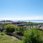 Haus mit Blick auf See und grüne Landschaft unter blauem Himmel.