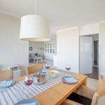 Esszimmer mit Tisch, Stühlen und Wein. Im Hintergrund Wohnzimmer mit Sofa und Glaswand.