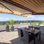 Terrasse mit Sitzgruppe, Sonnenschutz und Blick auf Wald und See.