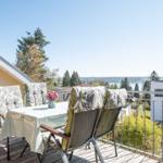Terrasse mit Tisch und Stühlen, Blick auf See und Bäume.