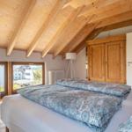 Schlafzimmer mit Holzdecke, Bett mit Muster, Kleiderschrank und Fensterblick