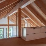Dachgeschoss mit Holzdecke, weißen Schränken und Blick in Wohnbereich.