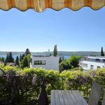 Terrasse mit Tisch und Stühlen, Blick auf See und Häuser unter blauem Himmel.